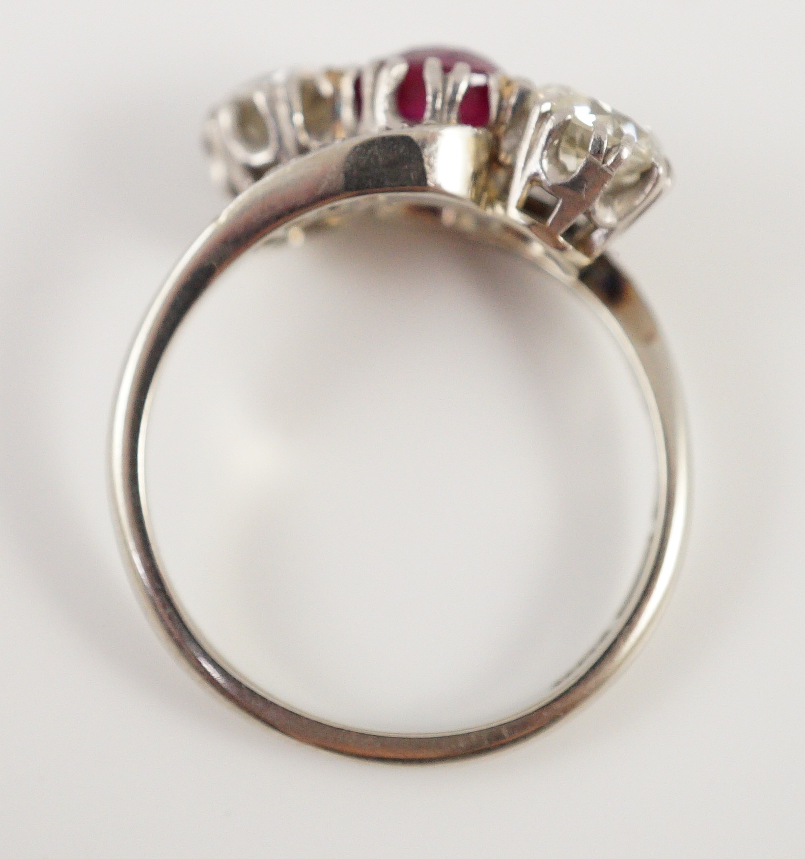 An 18ct white gold and platinum, two stone diamond and single stone synthetic? ruby set crossover ring, with diamond set shoulders